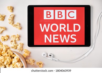 BBC World News logo on the screen of the tablet laying on the white table and sprinkled popcorn on it. Apple earphones near the tablet showing BBC app, August 2020, San Francisco, USA