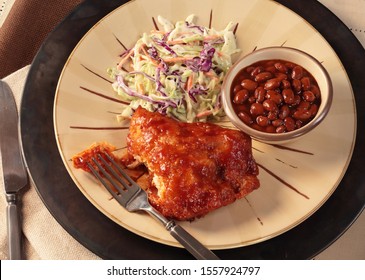 BBQ Chicken, Baked Beans And Coleslaw On Tan Plate And Fork.