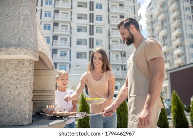 Bbq. Dad Grilling Meat While His Family Watching