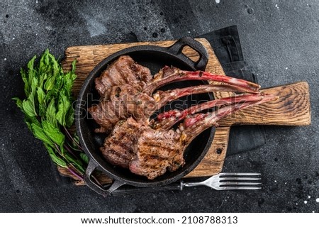 BBq Grilled lamb mutton chops steaks in a pan. Black background. Top view