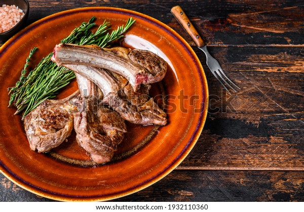 BBQ grilled lamb mutton\
meat chops steaks on a plate. Dark wooden background. Top view.\
Copy space.
