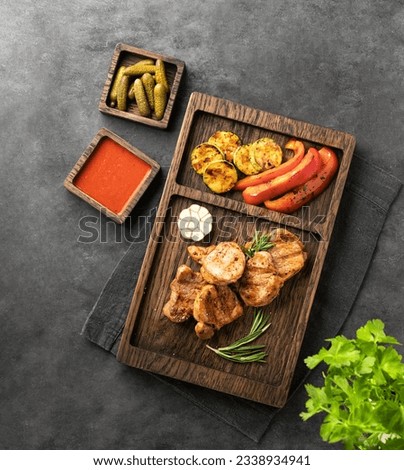 BBQ grilled pork fillet medallions with pepper, zucchini, rosemary and sauce on a wooden board on a dark background with fresh herb and snack. Top view and copy space.