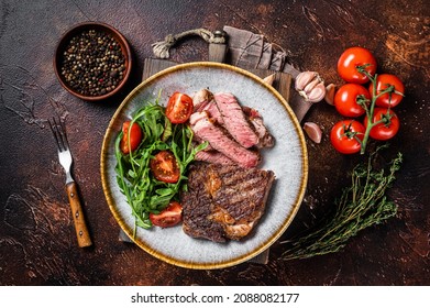BBQ Grilled rib eye steak, fried rib-eye beef meat on a plate with green salad. Dark background. top view - Shutterstock ID 2088082177