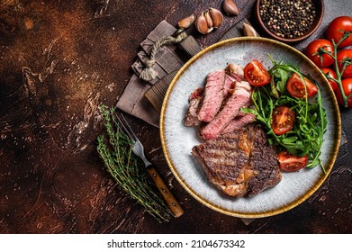 BBQ Grilled Rib Eye Steak, Fried Rib-eye Beef Meat On A Plate With Green Salad. Dark Background. Top View. Copy Space