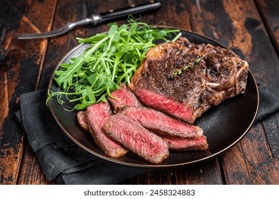 BBQ Grilled Wagyu New York beef meat steak or Striploin steak in a plate with salad. Wooden background. Top view.