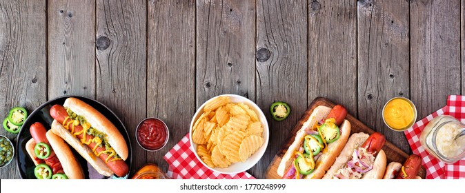 BBQ hot dog bottom border. Overhead view table scene with a dark wood banner background. Copy space.