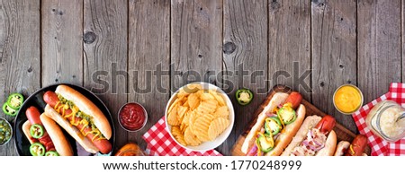 BBQ hot dog bottom border. Overhead view table scene with a dark wood banner background. Copy space.