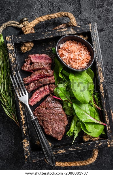 BBQ roasted flank steak in wooden\
tray with vegetable salad. Black background. Top\
view