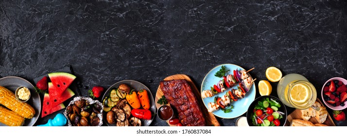 BBQ or summer picnic food border over a dark stone banner background. Assorted grilled meats, vegetables, fruits, salad and potatoes. Overhead view with copy space.