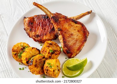 Bbq Tomahawk Pork Chops, Bone-in Steak With Grilled Corn Disks And Lime On White Plate On White Wooden Table, Horizontal View From Above, Close-up