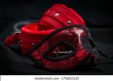 BDSM, Bondage Play, Fetish Wear And Kinky Sex Toy Concept With Close Up On Erotic Mask And Red Handcuffs Isolated On Black Silk Background