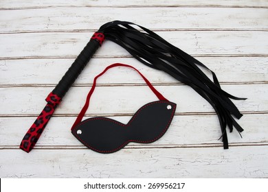 BDSM Toy, A black and red BDSM toy, a whip and mask over a distressed wood background