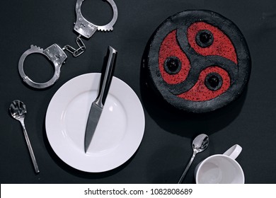 BDSM-themed cake with a white plate, a white cup, kitchen utensils and handcuffs, on dark background