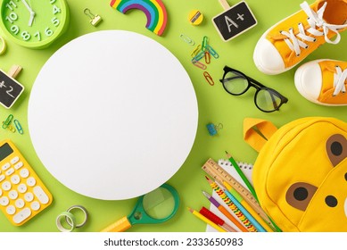 Be all set for elementary school. Top-view shot of backpack, assorted color pencils, A+ excellence badge, calculator, glasses, sneakers and more on light green backdrop with circle for text or promo