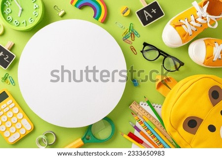 Be all set for elementary school. Top-view shot of backpack, assorted color pencils, A+ excellence badge, calculator, glasses, sneakers and more on light green backdrop with circle for text or promo