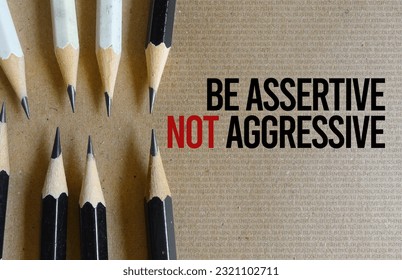 Be assertive not aggressive text written on recycle paper as background with black and white pencils