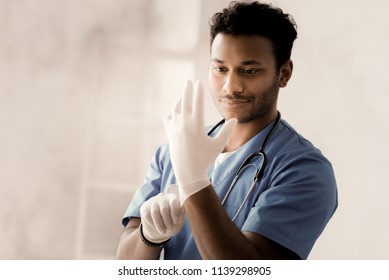 Be attentive. Positive medical worker keeping smile on his face while looking at his hand and standing over white background