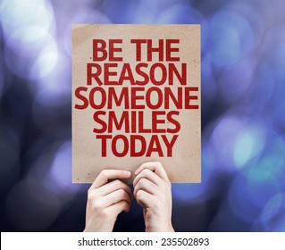 Be The Reason Someone Smiles Today card written on colorful background with defocused lights