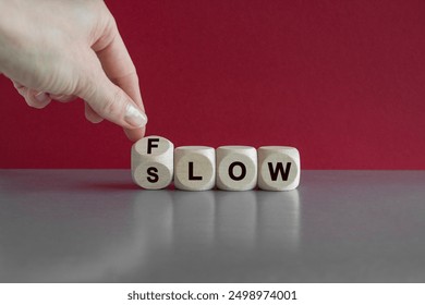 Be slow or in the flow. Businessman turns a cube and changes the word slow to flow. Beautiful grey table, red background, copy space. Business concept.