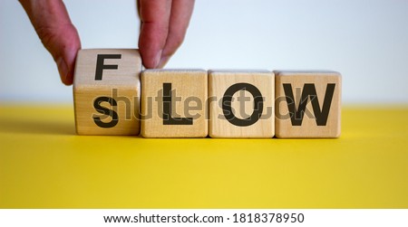 Be slow or in the flow. Male hand turns a cube and changes the word 'slow' to 'flow'. Beautiful yellow table, white background, copy space. Business concept.