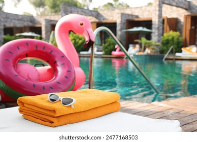 Beach accessories on sun lounger, inflatable ring and float near outdoor swimming pool at luxury resort, space for text - Powered by Shutterstock