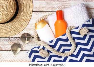 Beach Bag With Beach Accessories On A Wooden Background Top View. Beach Bag, Towel, Sunscreen, Glasses, Hat.
