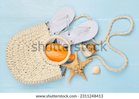 Beach bag with childish flip flops and sun protection on wooden background, top view