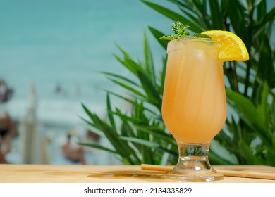 Beach bar concept. Drinking glass of orange punch cocktail with mint leaf and orange slice. Refreshing summer fruit cocktail, copy space. Summer sea resort. 