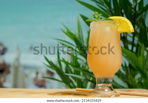 Beach bar concept. Drinking glass of\
orange punch cocktail with mint leaf and orange slice. Refreshing\
summer fruit cocktail, copy space. Summer sea resort.\
