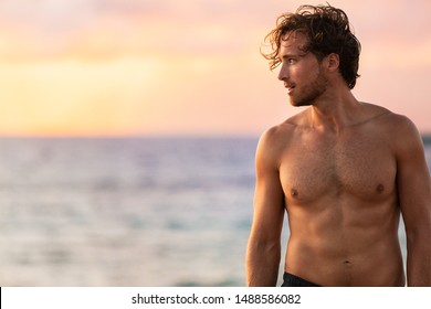 Beach body fit handsome man with six pack abs shirtless on summer Hawaii vacation sunset. Surfer lifestyle.