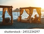 Beach cabana beds and sun loungers on the seashore at sunset.