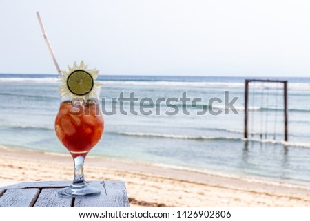 Beach cafe (bar). Red cocktail (bloody Mary) stands on a wooden table.  The sea in the background. Decoration drink - lime in the form of the sun. Recipe - Tomato juice, vodka, ice, salt. 