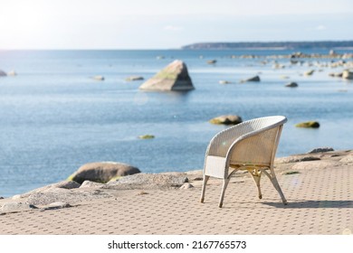 Beach cafe chair with blurred sea background. Summer vacation, travel, holidays concept. Lonely, empty, white wicker seat on shore pavement in sunshine. Seaside restaurant on sunny day. Soft focus