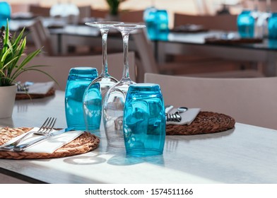 Beach cafe table setup on sunny day outdoor, served for lunch, blue glasses, wicker plates, cutlery. Authentic simple decor. Beautiful summer holiday concept. Romantic time at resort. Selective focus 