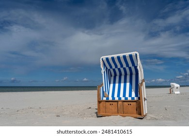 beach chair with blue and white fabric at the Baltic Sea in Prerow, Germany - the sun is shining, the sky is blue with vivid white clouds, a second beach chaor is in background