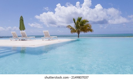 Beach Chair On The Shore Of An Infinity Pool Overlooking The Sea And Blue Sky In Summer In The Caribbean With Tropical Weather And No People, With Copy Space