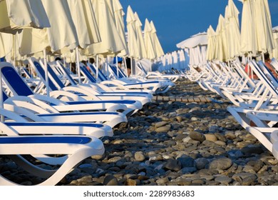 Beach chairs on a beach with a rocky shore with clear blue skies on a sunny day. Sun beds on the beach near the sea. Concept of summer holidays and recreation for tourism - Powered by Shutterstock