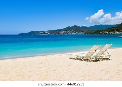 Beach chairs on white sandy beach in Grenada, the Caribbean.
Cruise ship in background.