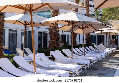 Beach Chairs, Umbrellas Around Swimming Pool With Palm Trees Background. Tourism, Summer Concept. Nice Beach Sun Beds With A White Towels. Empty Lounge Chair In A Row With Umbrella Under The Sunlight