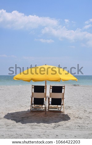 Beach chairs with yellow sun umbrella by the ocean.