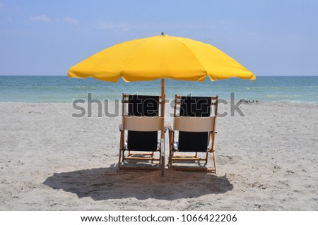 Beach chairs with yellow sun umbrella by the ocean.