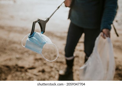 Beach Cleanup Volunteer Picking Up Face Mask For Environment Campaign