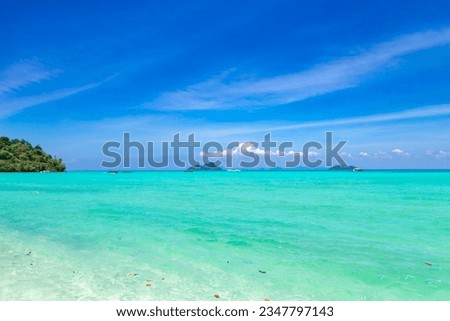 A beach with clear turquoise water, tropical green islands and a blue sky with a few white clouds
