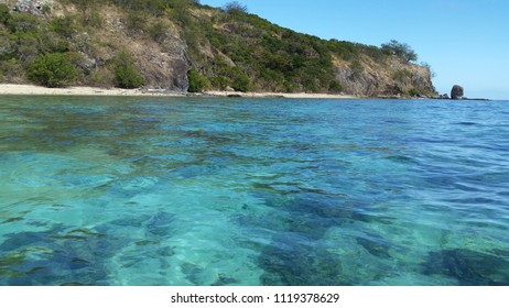 Beach and clear turquoise waters of the Pacific Ocean on the coast of a Fijian island with reef showing below water on a sunny summer day