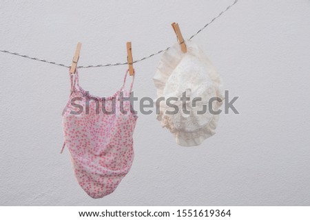 Baby’s beach clothes drying on a clothesline. Tiny white Panama hat and pink bikini on white background.
