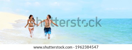 Beach couple Caribbean vacation summer travel fun splashing water running in fit bikini body. Happy tourists relaxing laughing enjoying paradise holiday banner panoramic.