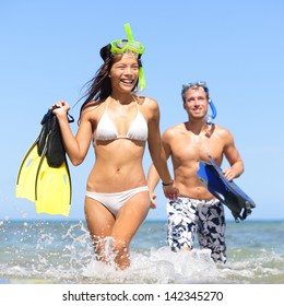 Beach Couple Having Fun On Vacation Travel With Snorkel, Mask And Fins. Happy Interracial Multi-ethnic Young Couple Running Excited At Tropical Beach During Summer Holidays At Maui, Hawaii, USA