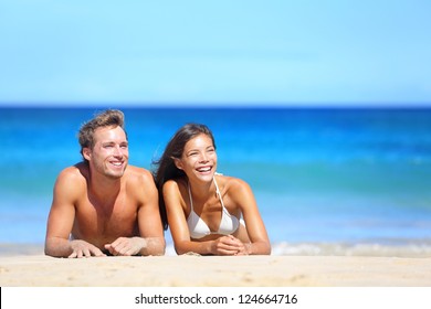 Beach couple looking. Happy multi-ethnic young couple lying on sand under sunny summer sun. Travel holidays concept. Caucasian man, Asian woman on hawaii. - Powered by Shutterstock