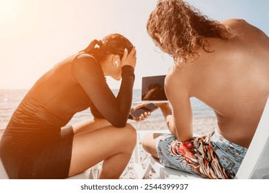 Beach Couple Tablet Sun; Two people sit on beach chairs and look at a tablet together on a sunny day. - Powered by Shutterstock