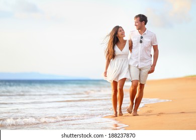 Beach Couple Walking On Romantic Travel Honeymoon Vacation Summer Holidays Romance. Young Happy Lovers, Asian Woman And Caucasian Man Holding Hands Embracing Outdoors.